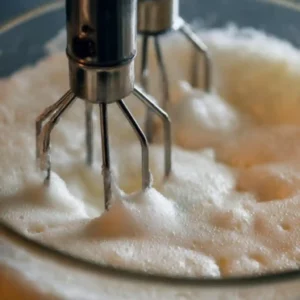 Electric beaters whipping egg whites to soft peaks for a sugar-free lemon blueberry pudding cake.