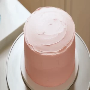 Labubu Cakes: Unique Designs, Flavors & Celebration Treats 8 Frosting a layered Labubu cake with creamy vanilla icing using a spatula.