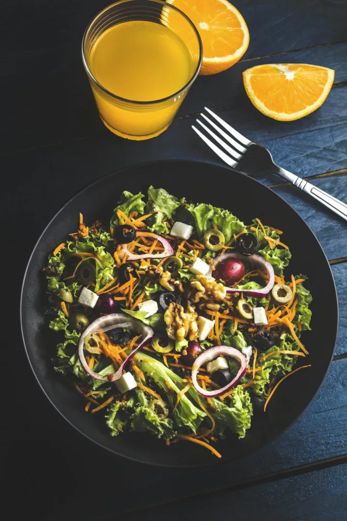 Pegan Diet 2026: A No-Nonsense Beginner Guide 2 Pegan diet simple plate with leafy greens, olives, red onion, walnuts, shredded carrots, feta cheese, and fresh orange juice.