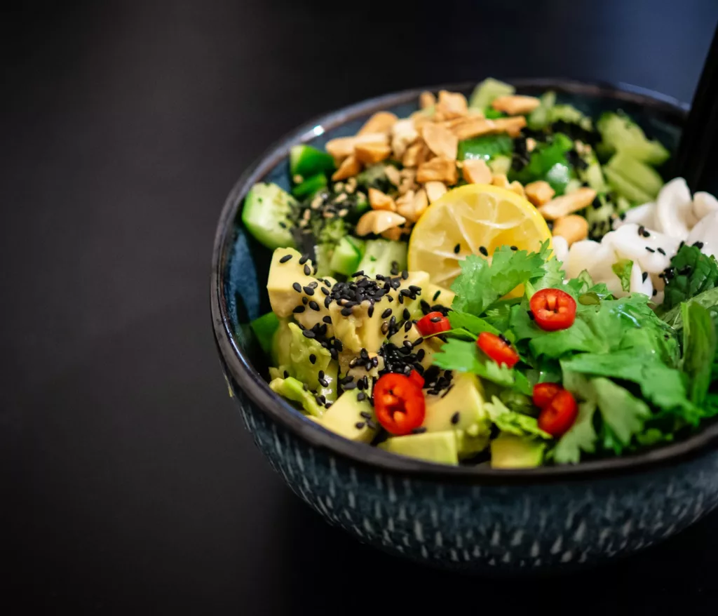 Pegan Diet 2026: A No-Nonsense Beginner Guide 4 Pegan diet bowl with avocado, fresh vegetables, lemon, sesame seeds, herbs, and clean protein in a dark ceramic bowl.