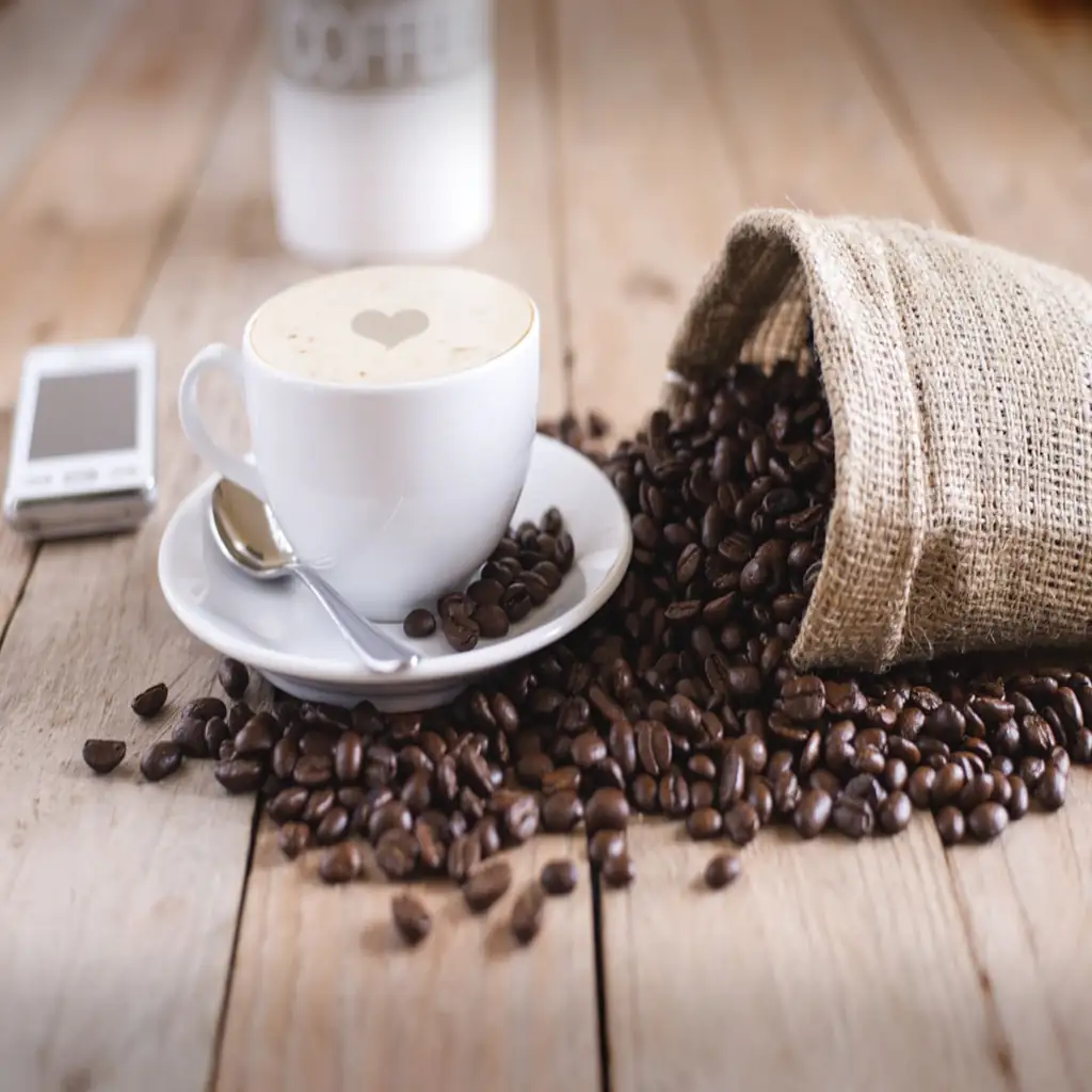 Hot black coffee cup with coffee beans on a wooden table beside a notebook in a cozy workspace setting.