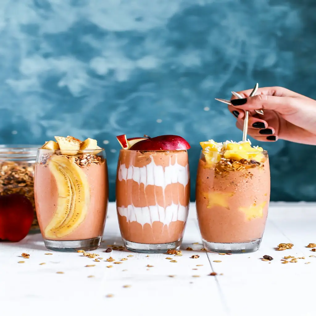 Healthy protein smoothies with fruit toppings served on a kitchen counter with granola and fresh ingredients.