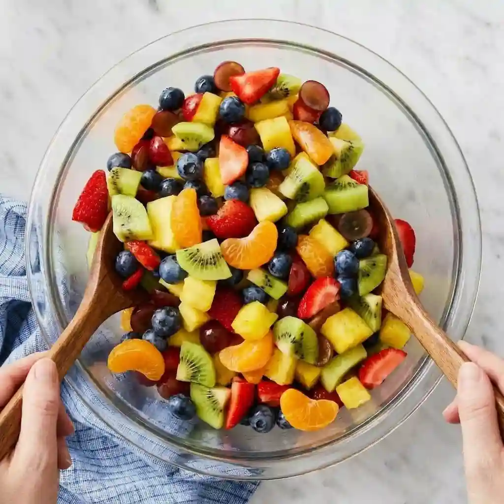 Fresh mixed fruit salad with strawberries, blueberries, kiwi, grapes, pineapple, and mandarin oranges in a glass bowl.