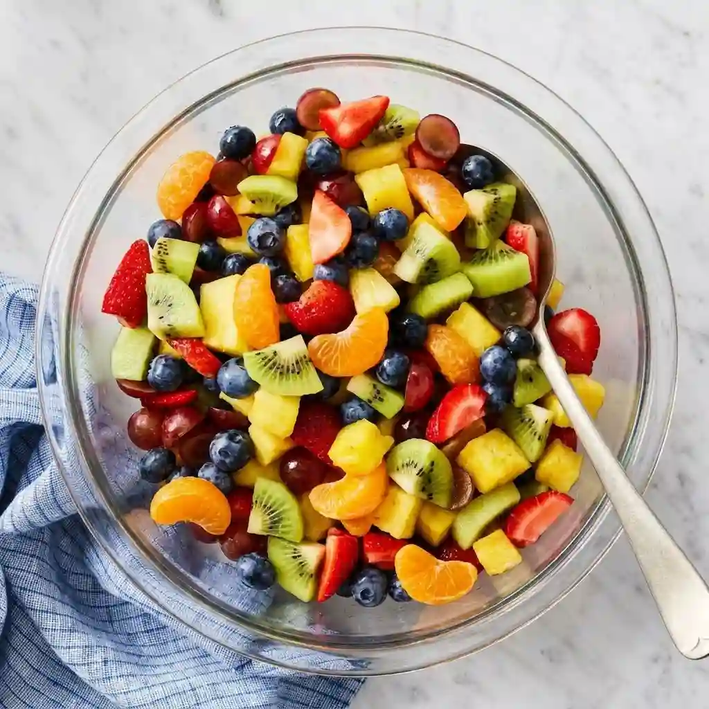 Colorful fresh fruit salad with strawberries, kiwi, blueberries, grapes, pineapple, and mandarin oranges served in a glass bowl.