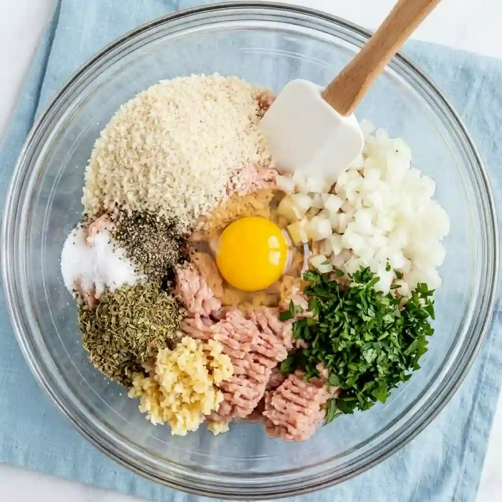 raw turkey meatball mixture with egg breadcrumbs garlic onion parsley in glass bowl